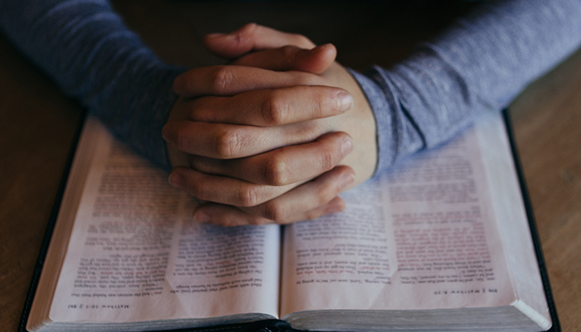 Hands praying on top of a Bible